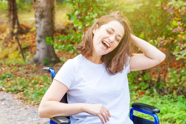 Mladá žena se šťastným handicapem na vozíčku v nemocničním parku si užívá svobody. Paralyzovaná dívka v invalidním křesle pro tělesně postižené v přírodě. Rehabilitační koncept. — Stock fotografie