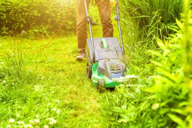 Bahçede çim biçme makinesiyle çim biçen bir adam. Bahçe işleri kırsal yaşam tarzı. Güneş ışığında taze yeşil çimlerin manzarası baharda ya da yaz mevsiminde bahçe manzarası.