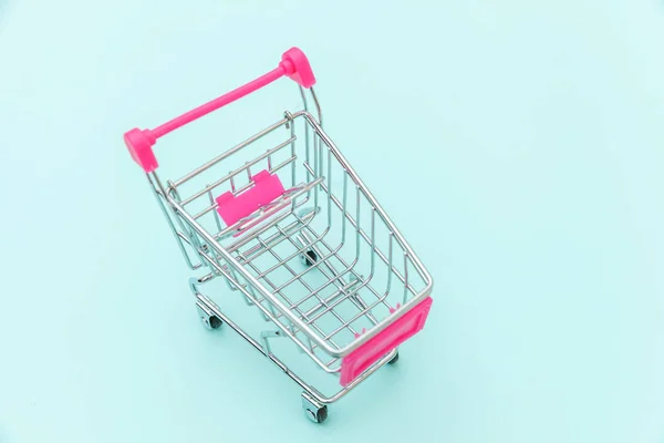 Malý nákupní vozík s potravinami pro nákupní hračky s kolečky izolovanými na modrém pastelově barevném trendy pozadí Kopírovat prostor. Prodej koupit nákupní centrum obchod spotřebitelský koncept. — Stock fotografie