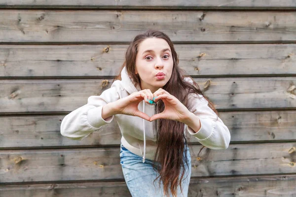 Love, heart shape, peace. Beauty portrait young happy positive woman showing heart sign with hands on wooden wall background