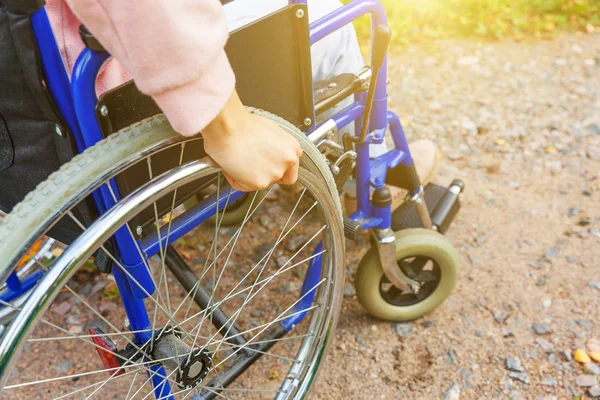 Hand handicap woman in wheelchair wheel on road in hospital park waiting for patient services. Unrecognizable paralyzed girl in invalid chair for disabled people outdoors. Rehabilitation concept.