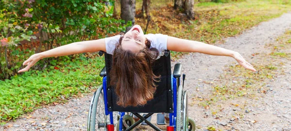 Молодая счастливая женщина-инвалид в инвалидной коляске на дороге в больничном парке наслаждается свободой. Парализованная девочка в инвалидном кресле для инвалидов на природе. Концепция реабилитации. — стоковое фото