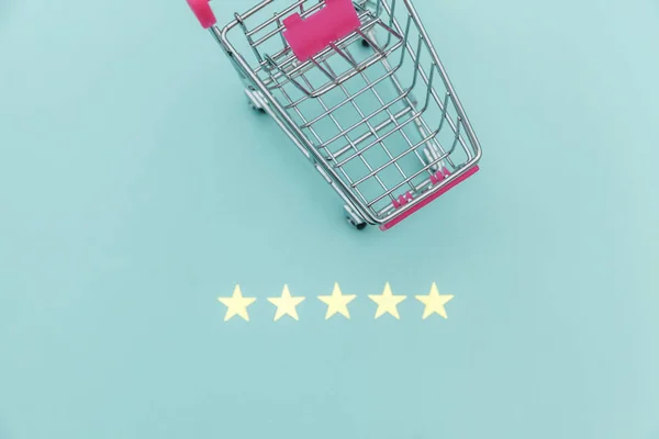 Malý supermarket nákupní vozík pro nákupy hraček s kolečky a 5 hvězdiček hodnocení izolované na pastelově modrém pozadí. Maloobchodní spotřebitel nákup on-line posouzení a přezkoumání koncepce. — Stock fotografie