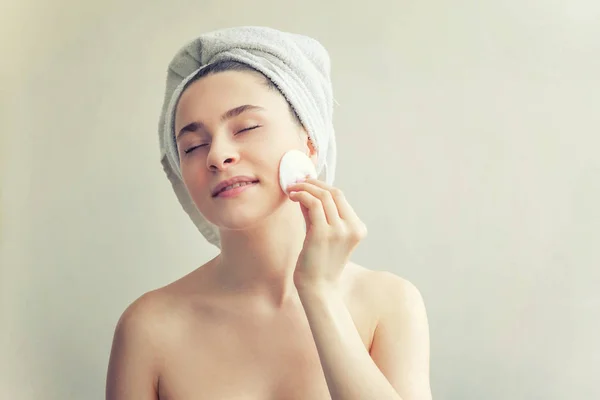 Lachende vrouw in handdoek op hoofd met zachte gezonde huid verwijderen make-up met wattenschijfje geïsoleerd op witte achtergrond — Stockfoto