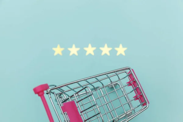 Small supermarket grocery push cart for shopping toy with wheels and 5 stars rating isolated on pastel blue background. Retail consumer buying online assessment and review concept.