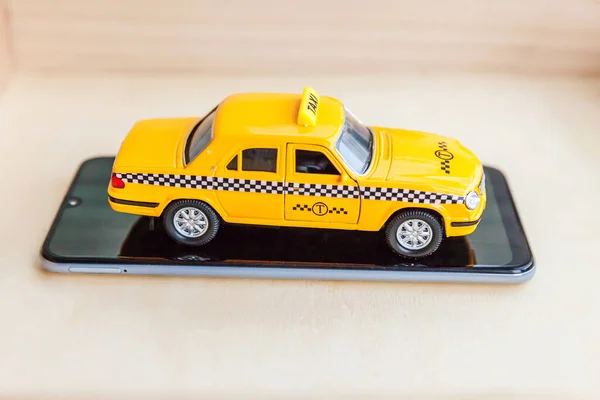 Aplicația smartphone a serviciului de taxi pentru căutarea online a conceptului de cabină de apel și rezervare. Pur și simplu proiectați mașină de jucărie galbenă Taxi Cab pe ecranul gol al telefonului inteligent pe fundal din lemn. Simbolul taxiului . — Fotografie, imagine de stoc