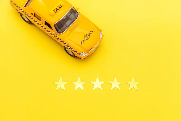 Yellow toy car Taxi Cab and 5 stars rating isolated on yellow background. Smartphone application of taxi service for online searching calling and booking cab concept. Taxi symbol. Copy space.