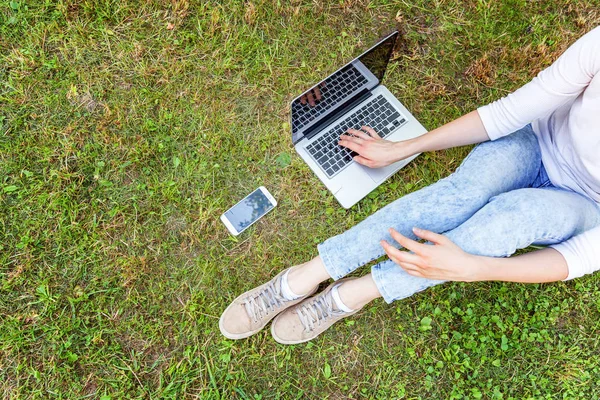 Женские ноги на зеленой газоне в городском парке, руки работают на ноутбуке. Концепция внештатного бизнеса — стоковое фото