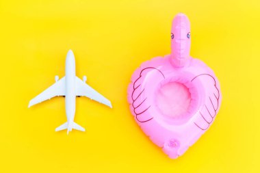 Yaz kumsalı kompozisyonu. Uçak ve sarı zemin üzerinde izole edilmiş şişirilebilir flamingo ile minimum basit düz yatıyordu. Seyahat macerası konsepti. Üst görünüm kopyalama alanı.