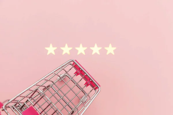 Malý supermarket nákupní vozík pro nákupy hraček s kolečky a 5 hvězdiček hodnocení izolované na pastelově růžovém pozadí. Maloobchodní spotřebitel nákup on-line posouzení a přezkoumání koncepce. — Stock fotografie