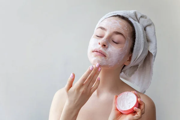 Retrato de belleza de mujer en toalla en la cabeza con máscara blanca nutritiva o crema en la cara, fondo blanco aislado. Limpieza de la piel ecológico cosmético spa relajante concepto. —  Fotos de Stock