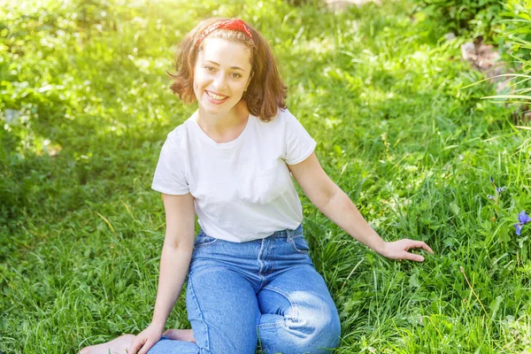 Menina feliz sorrindo ao ar livre. Mulher bonita morena jovem com cabelos castanhos descansando no parque ou jardim fundo de grama verde. Mulher europeia. Emoção humana positiva expressão facial linguagem corporal . — Fotografia de Stock