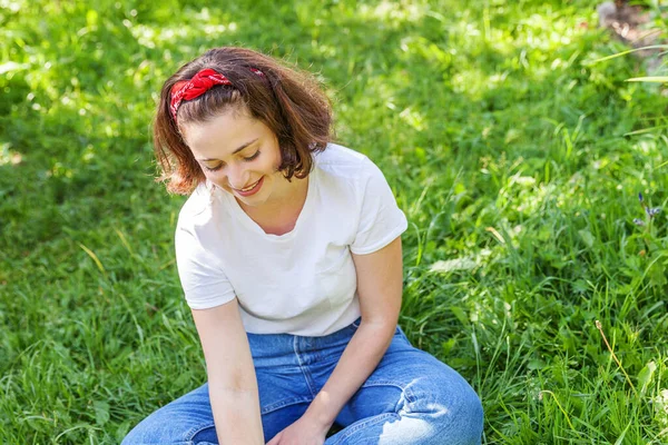 Šťastná dívka se usmívá venku. Krásná mladá brunete žena s hnědými vlasy odpočívá na parku nebo na zahradě zelená tráva pozadí. Evropanka. Pozitivní lidské emoce výraz obličeje řeč těla. — Stock fotografie