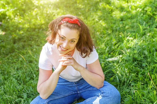 야외에서 미소짓는 행복 한 소녀. 갈색 털을 가진 아름다운 젊은 브루 네 테 여인은 공원이나 푸른 잔디 위에 앉아 있다. 유럽 여성. 긍정적 인 인간의 표정 표정 표정 표정. — 스톡 사진