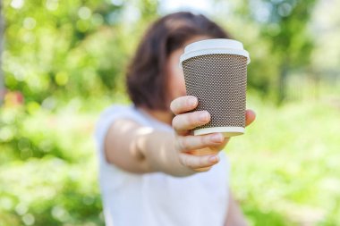 Happy girl smiling outdoor having lunch break. Beautiful young brunete woman with take away coffee cup resting on park or garden green background. Education freelancer resting leisure concept.