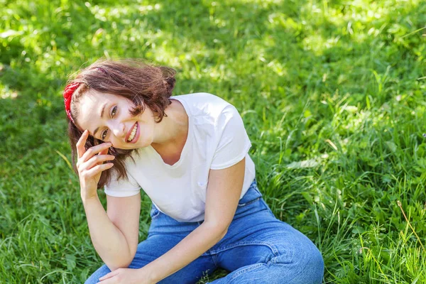 Šťastná dívka se usmívá venku. Krásná mladá brunete žena s hnědými vlasy odpočívá na parku nebo na zahradě zelená tráva pozadí. Evropanka. Pozitivní lidské emoce výraz obličeje řeč těla. — Stock fotografie