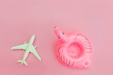 Yaz kumsalı kompozisyonu. Uçak ve pastel pembe arka planda izole edilmiş şişme flamingo ile minimum sade düz yatıyordu. Seyahat macerası konsepti. Üst görünüm kopyalama alanı.