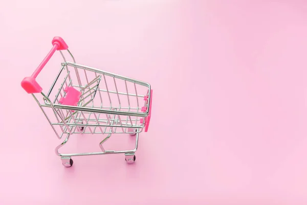 Malý nákupní vozík pro nakupování hraček s koly izolovanými na růžovém pastelově barevném pozadí. Prodej koupit nákupní centrum obchodní dílny. Kopírovat místo. — Stock fotografie