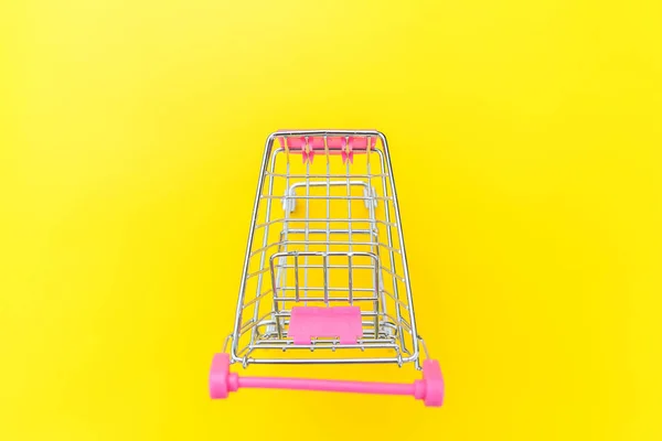 Small supermarket grocery push cart for shopping toy with wheels isolated on yellow colourful trendy modern fashion background. Sale buy mall market shop consumer concept. Copy space.