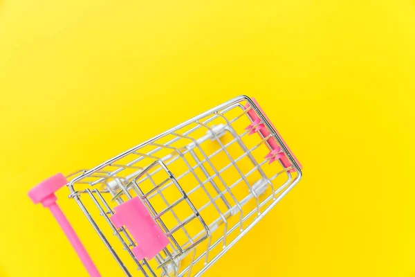 Small supermarket grocery push cart for shopping toy with wheels isolated on yellow colourful trendy modern fashion background. Sale buy mall market shop consumer concept. Copy space. — Stock Photo, Image