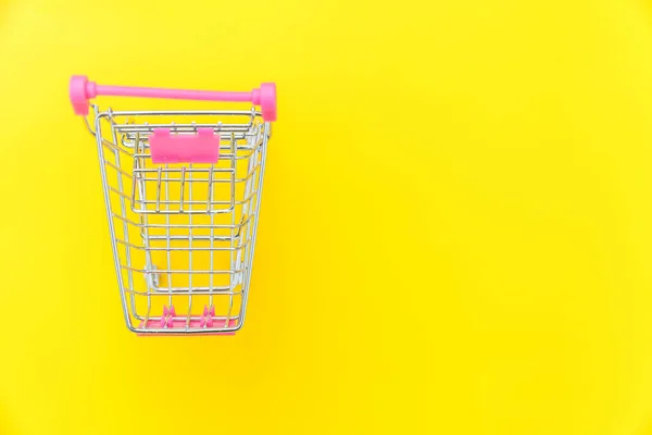 Small supermarket grocery push cart for shopping toy with wheels isolated on yellow colourful trendy modern fashion background. Sale buy mall market shop consumer concept. Copy space. — Stock Photo, Image