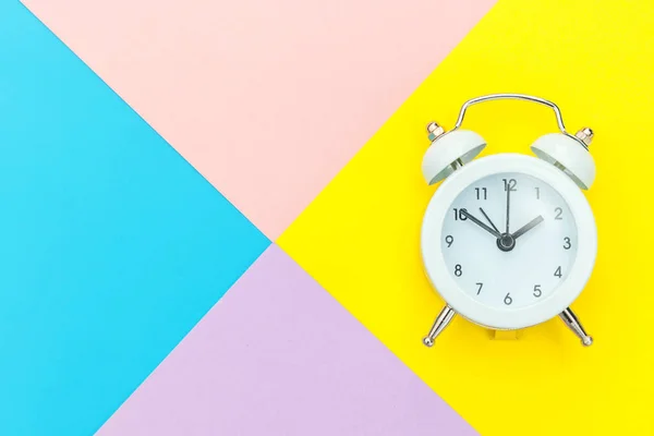 青い黄色のピンクのパステルカラーの幾何学的背景に隔離されたツインベル古典的な目覚まし時計を鳴らす。人生の残りの時間良い朝の夜の目覚めの概念を覚ます。フラットレイアウトトップビューコピースペース. — ストック写真