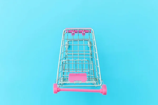 Small supermarket grocery push cart for shopping toy with wheels isolated on blue pastel colorful trendy background Copy space. Sale buy mall market shop consumer concept.