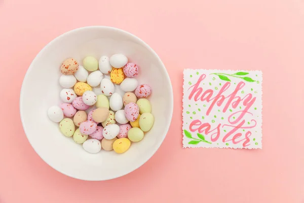 Inscription HAPPY EASTER letters candy chocolate eggs and jellybean sweets isolated on trendy pastel pink background. Simple minimalism flat lay top view copy space