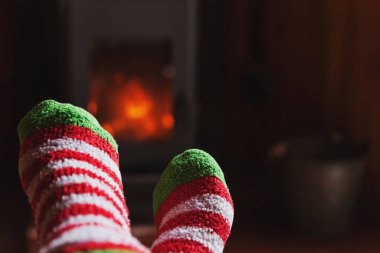 Kış kıyafetlerinin içinde ayaklar şömine arkasında yün çoraplar. Kadın kış ya da sonbahar akşamları evde oturup dinleniyor ve ısınıyor. Kış ve soğuk hava kavramı. Hygge Noel arifesi.