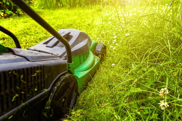 Man klipper grönt gräs med gräsklippare i trädgården. Trädgårdsskötsel land livsstil bakgrund. Vacker utsikt över färsk grön gräsmatta i solljus, trädgård landskap på våren eller sommaren. — Stockfoto