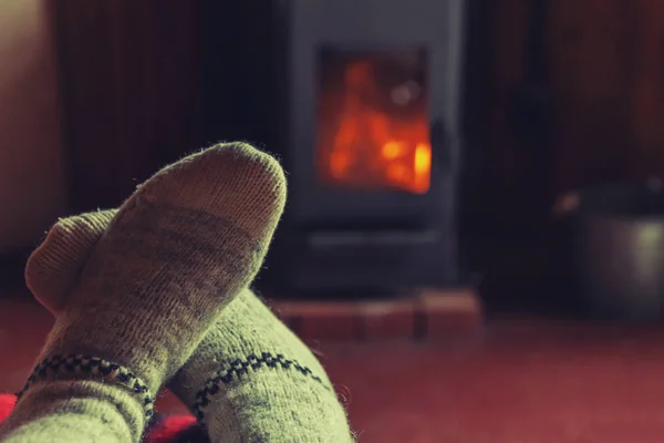 Feet legs in winter clothes wool socks at fireplace background. Woman sitting at home on winter or autumn evening relaxing and warming up. Winter and cold weather concept. Hygge Christmas eve.