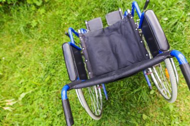 Hastane parkında çimlerde bekleyen boş tekerlekli sandalye hasta hizmetlerini bekliyor. Doğada park etmiş engelliler için geçersiz sandalye. Özürlü erişilebilir sembol. Sağlık hizmeti tıbbi konsepti.