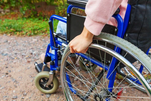 Hand handicap woman in wheelchair wheel on road in hospital park waiting for patient services. Unrecognizable paralyzed girl in invalid chair for disabled people outdoors. Rehabilitation concept.