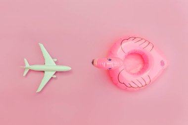 Yaz kumsalı kompozisyonu. Uçak ve pastel pembe arka planda izole edilmiş şişme flamingo ile minimum sade düz yatıyordu. Seyahat macerası konsepti. Üst görünüm kopyalama alanı.