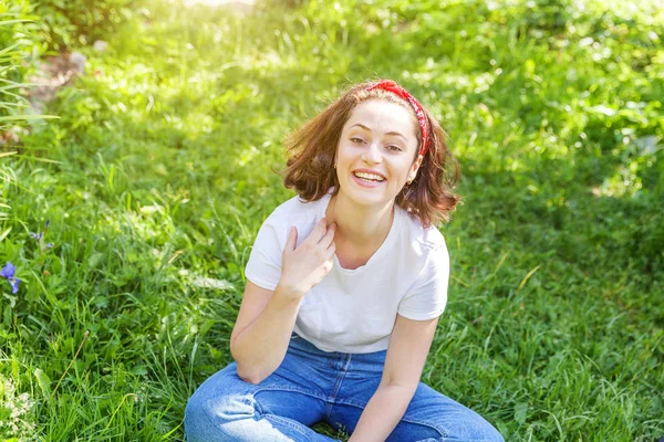 Menina feliz sorrindo ao ar livre. Mulher bonita morena jovem com cabelos castanhos descansando no parque ou jardim fundo de grama verde. Mulher europeia. Emoção humana positiva expressão facial linguagem corporal . — Fotografia de Stock