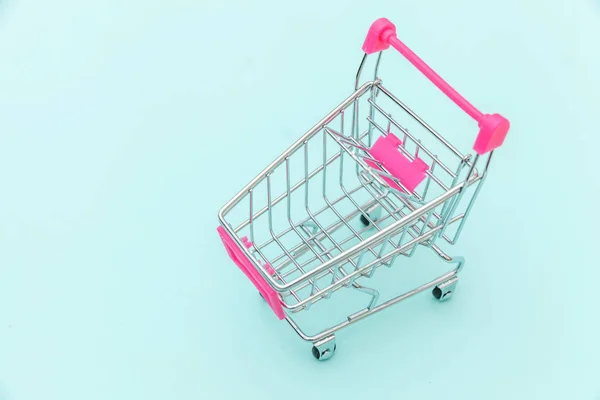 Petit supermarché épicerie poussette chariot pour jouet shopping avec roues isolées sur fond bleu pastel coloré tendance Copier l'espace. Vente acheter centre commercial marché boutique concept de consommateur. — Photo
