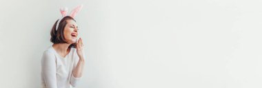 Mutlu Paskalya bayramı bahar kutlamaları. Beyaz arka planda izole edilmiş tavşan kulağı takan genç bir kadın. Tatil için hazırlık. Kız mutlu ve heyecanlı görünüyor, Paskalya günü eğleniyor. Pankart