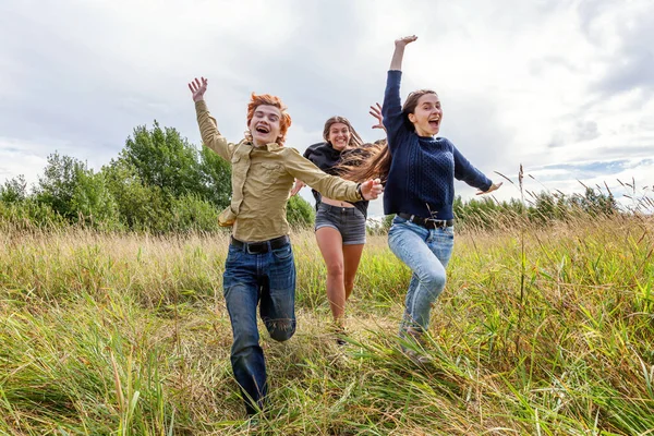 Летние каникулы праздник счастливые люди концепции. Группа из трех друзей мальчик и две девочки бегают и веселятся вместе на открытом воздухе. Пикник с друзьями на природе. — стоковое фото