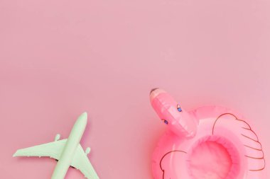 Yaz kumsalı kompozisyonu. Uçak ve pastel pembe arka planda izole edilmiş şişme flamingo ile minimum sade düz yatıyordu. Seyahat macerası konsepti. Üst görünüm kopyalama alanı.