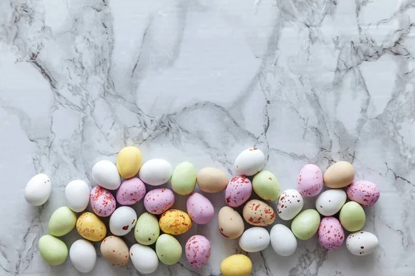 Happy Easter concept. Preparation for holiday. Easter pastel candy chocolate eggs sweets on trendy gray marble background. Simple minimalism flat lay top view copy space