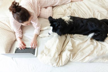 Mobil Ofis evde. Evcil köpekle pijamalı genç bir kadın evdeki bilgisayarda çalışıyor. Yaşam tarzı kızı içeride ders çalışıyor. Serbest ticaret karantina kavramı