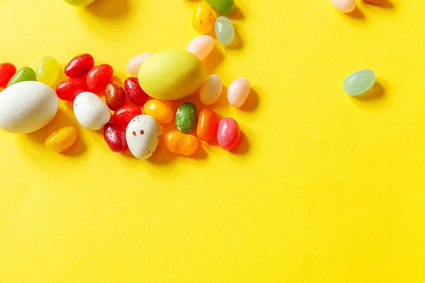 Happy Easter concept. Preparation for holiday. Easter candy chocolate eggs and jellybean sweets isolated on trendy yellow background. Simple minimalism flat lay top view copy space