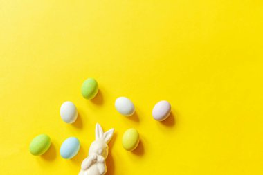 Mutlu Paskalyalar. Tatil için hazırlık. Paskalya çikolatalı yumurta, tatlı ve sarı arka planda izole edilmiş tavşan oyuncağı. Basit minimalizm düz üst görünüm kopyalama alanı