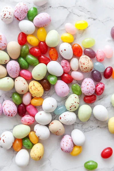 Happy Easter concept. Preparation for holiday. Easter candy chocolate eggs and jellybean sweets on trendy gray marble background. Simple minimalism flat lay top view copy space