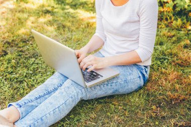 Serbest iş kavramı. Kadın ayak dizüstü pc bilgisayar üzerinde çalışan Şehir Parkı yeşil çim çim üzerinde. Yaşam tarzı otantik samimi öğrenci kız açık havada okuyor. Mobil ofis