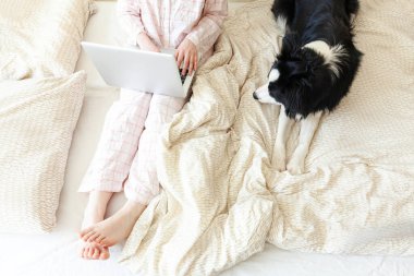 Mobil Ofis evde. Evcil köpekle pijamalı genç bir kadın evdeki bilgisayarda çalışıyor. Yaşam tarzı kızı içeride ders çalışıyor. Serbest ticaret karantina kavramı