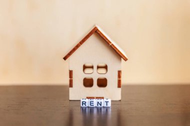 Minyatür oyuncak model evi. Üzerinde tahta zemin üzerine yazılmış RENT harfleri var. Eco Village soyut çevre geçmişi. Gayrimenkul ipoteği sigortası tatlı ev ekoloji kira kavramı