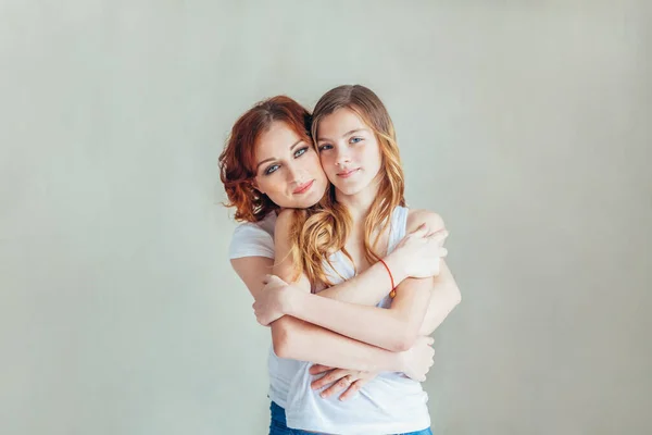 Stay at home mom, stay safe. Young mother embracing her child. Woman and teenage girl relaxing in white bedroom near gray wall indoors. Happy family at home. Young mom playing whith her daughter