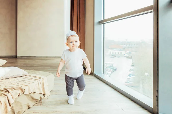 Quédese en casa. Pequeña niña bebé dulce lindo que se queda cerca de la ventana grande en la sala de estar de luz brillante en el hogar en interiores. Niñez familia maternidad ternura concepto . — Foto de Stock