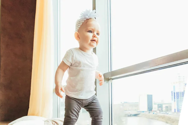 집에서 안전을 유지하라. 작고 귀여운 작은 아기 아기가 큰 창문 가까이 집 안의 밝은 밝은 거실에 머물고 있습니다. 어린 시절의 가정 분만 의부드러운 개념. — 스톡 사진